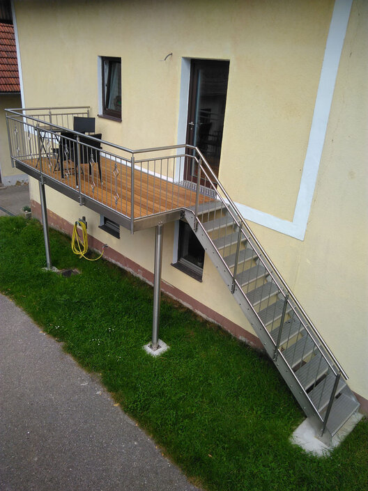 Gelbes Haus mit Edelstahlstiege und Balkon auf Säulen aus Metall