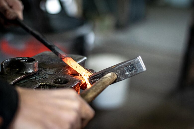Schmiedeprodukte Kunstschmied Oberösterreich Jemand schlägt mit dem Hammer auf ein glühendes Stück Metall auf einem Amboss