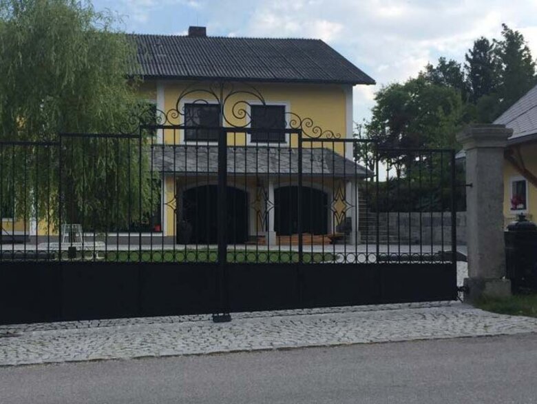 Geschmiedetes Einfahrtstor Außenansicht eines geschmiedeten Einfahrtstores vor einem gelben Haus